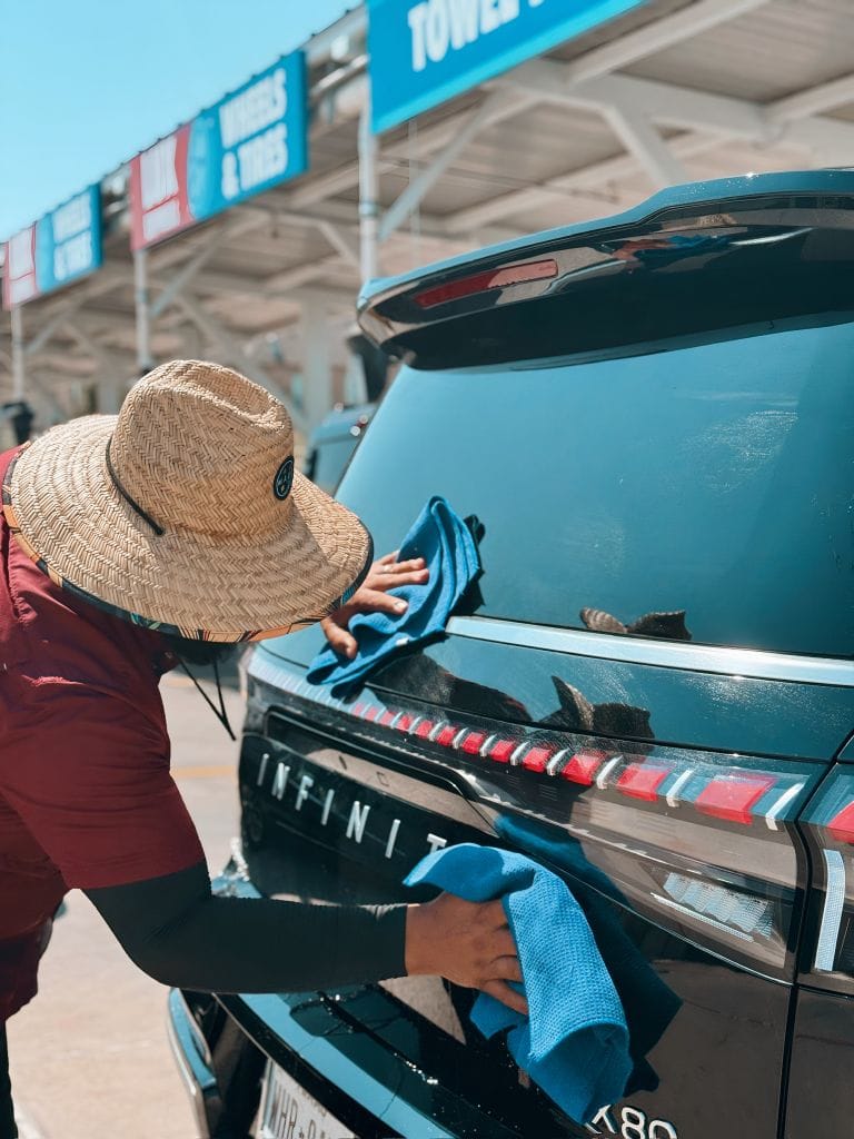Brightworks Fort Worth team member wiping down the rear of a black Infiniti QX80 SUV
