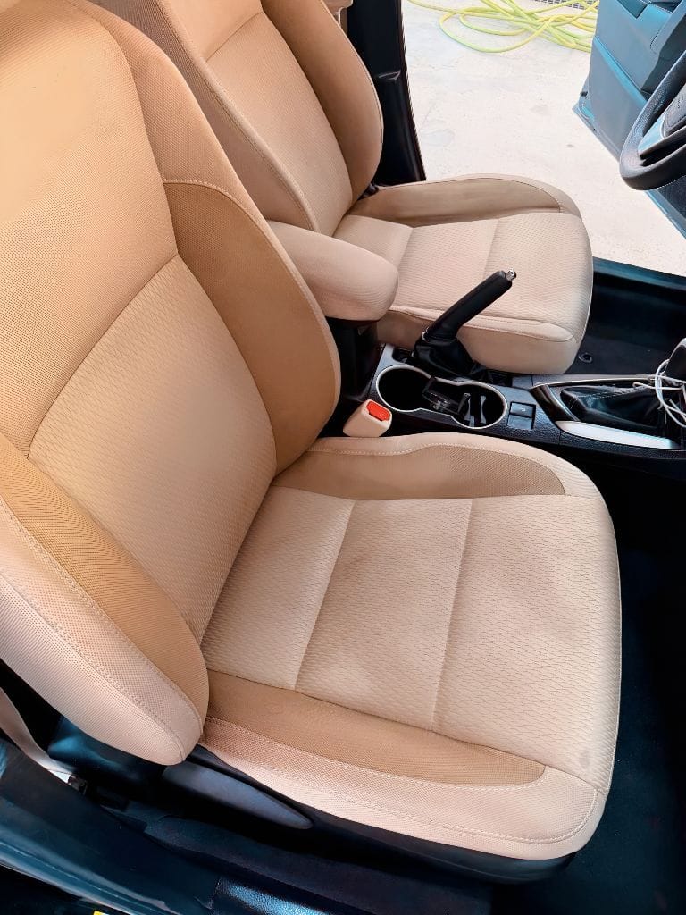 Spotlessly cleaned tan fabric front seats and center console of a vehicle detailed at Brightworks Fort Worth