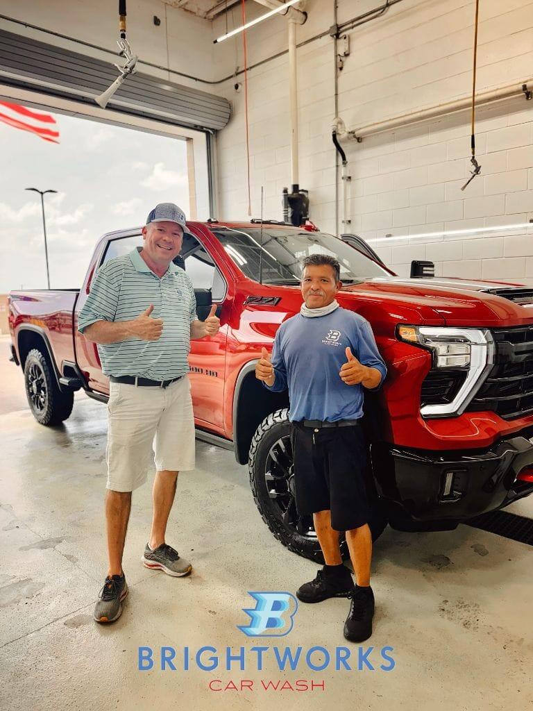 Brightworks Fort Worth owner and team member giving two thumbs up in front of a freshly detailed red Silverado 2500 HD