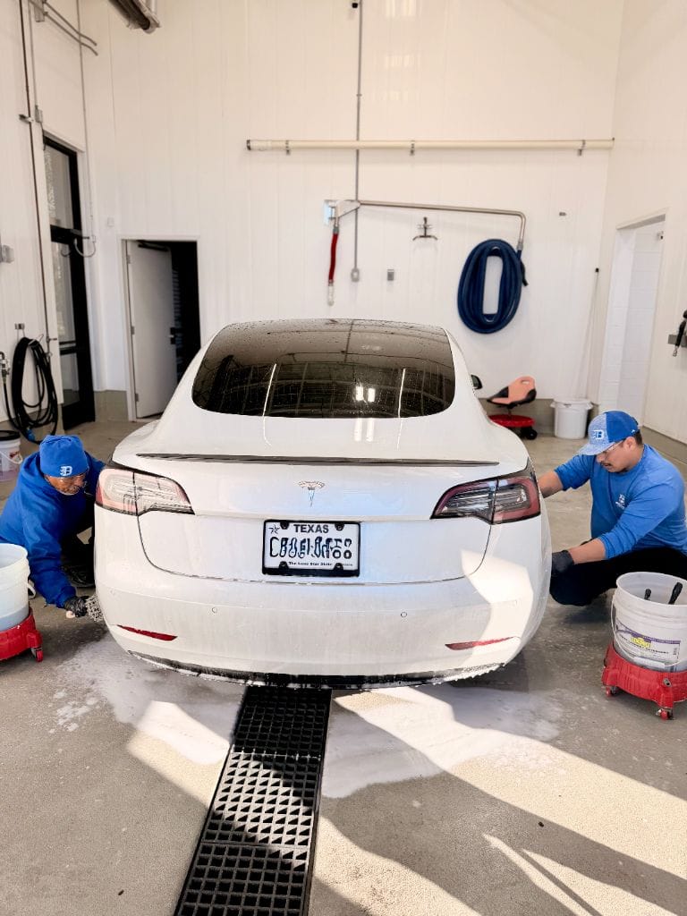 Two Brightworks Fort Worth detailers scrubbing the rear bumper and lower panels of a white Tesla Model 3 with two-bucket method