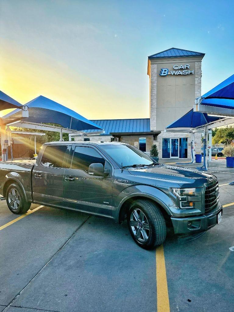 Graphite Ford F-150 parked at Brightworks Granbury at golden-hour sunset with the Car Wash tower sign lit up