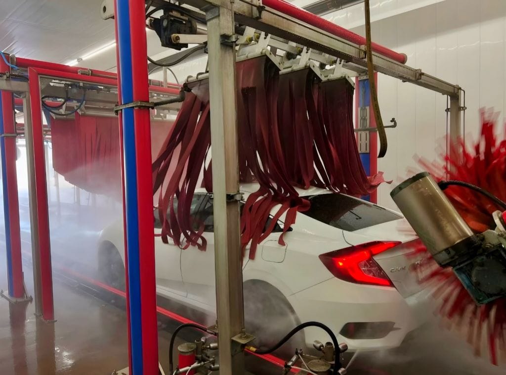 Brightworks Granbury exterior wash — white Honda Civic passing under hanging curtain strips with steam and side brush