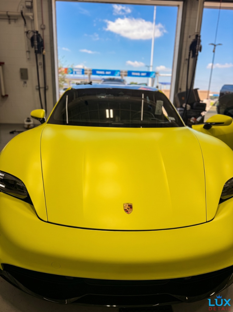 Yellow Porsche Taycan front end showing flawless paint after full detail at Brightworks — sunny day in detail bay