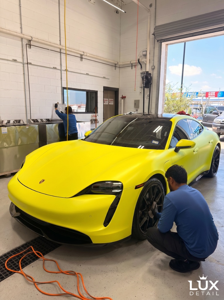 Brightworks team members performing a full detail on a yellow Porsche Taycan — wheel cleaning and exterior work in progress
