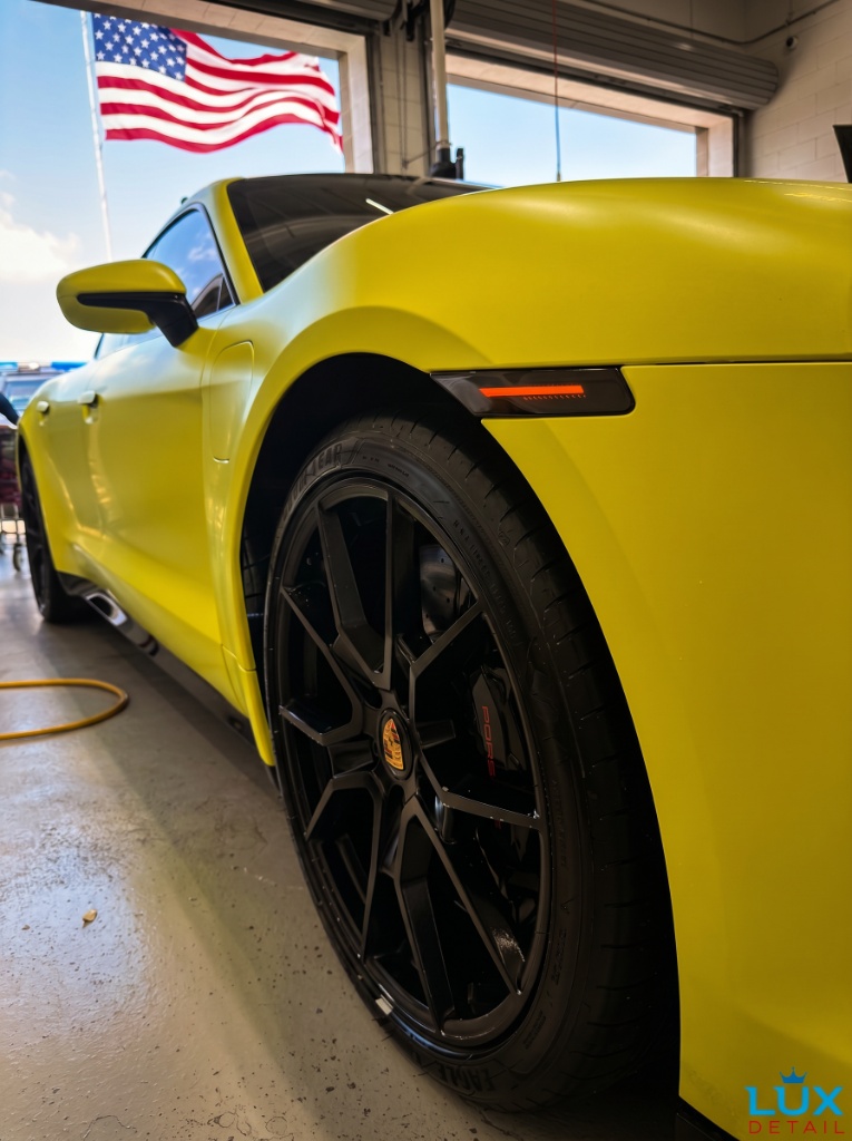 Yellow Porsche 911 GT3 wheel and Brembo brake caliper detail at Brightworks — American flag in background