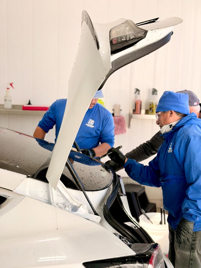 Brightworks team members in blue uniforms carefully cleaning a Tesla's exterior — screen-safe products and expert interior care